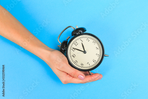  Beautiful young woman's hands with alarm clock on pastel background.