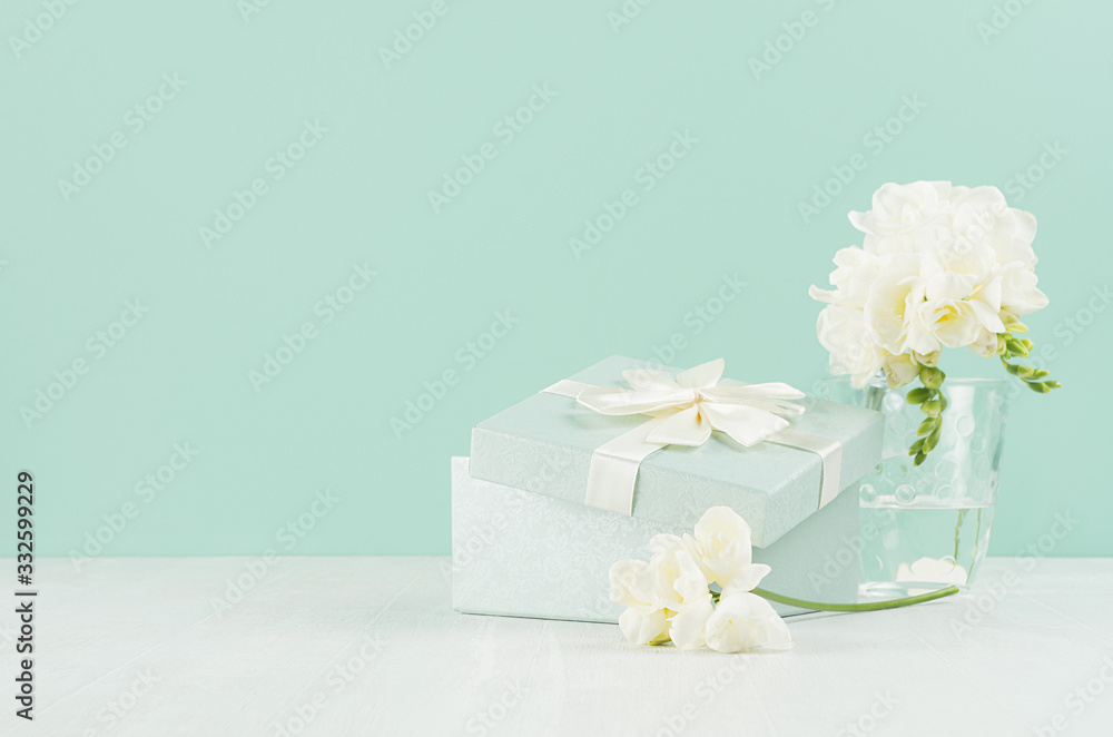 Wedding festive background with gift box, fragrance soft white flowers freesia in bouquet in glass vase in green mint menthe interior on white wood board.