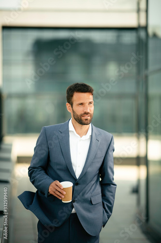 Young handsome man drinking coffee outdoors. Businessman in a blue suit.