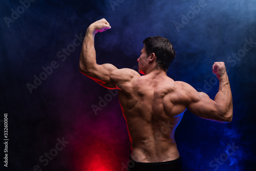 Muscular man showing muscles isolated on the black background with colored smoke. Concept of healthy lifestyle  © Hladchenko Viktor