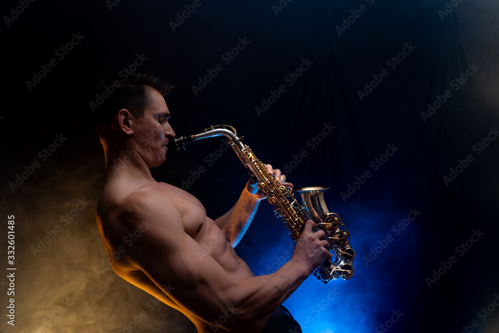 Naklejka premium Muscular man with naked torso playing on saxophone with smoked colorful background 