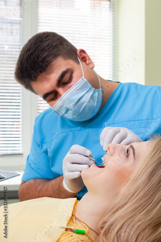 Dentist examining patient s teeth  wearing blue uniform and gloves  looking at patient s teeth carefully with dental instruments