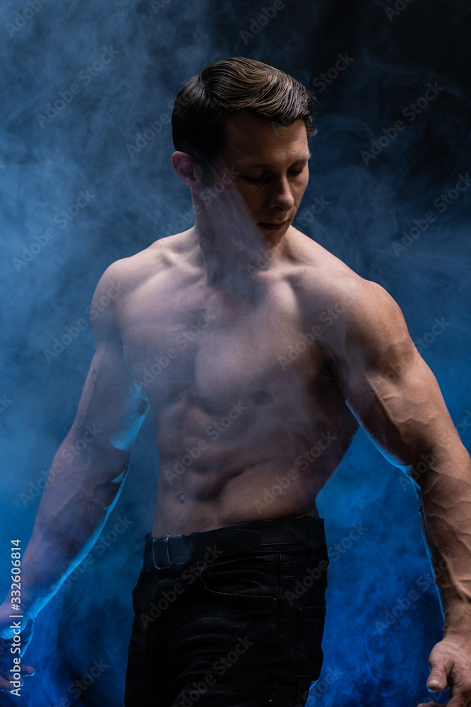 Fototapeta premium Muscular man showing muscles isolated on the black background with colored smoke. Concept of healthy lifestyle 