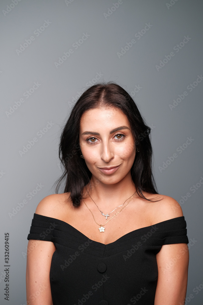 Obraz premium A large portrait of a middle-aged woman (30-35 years old) with dark hair and brown eyes in a black dress on a light background.