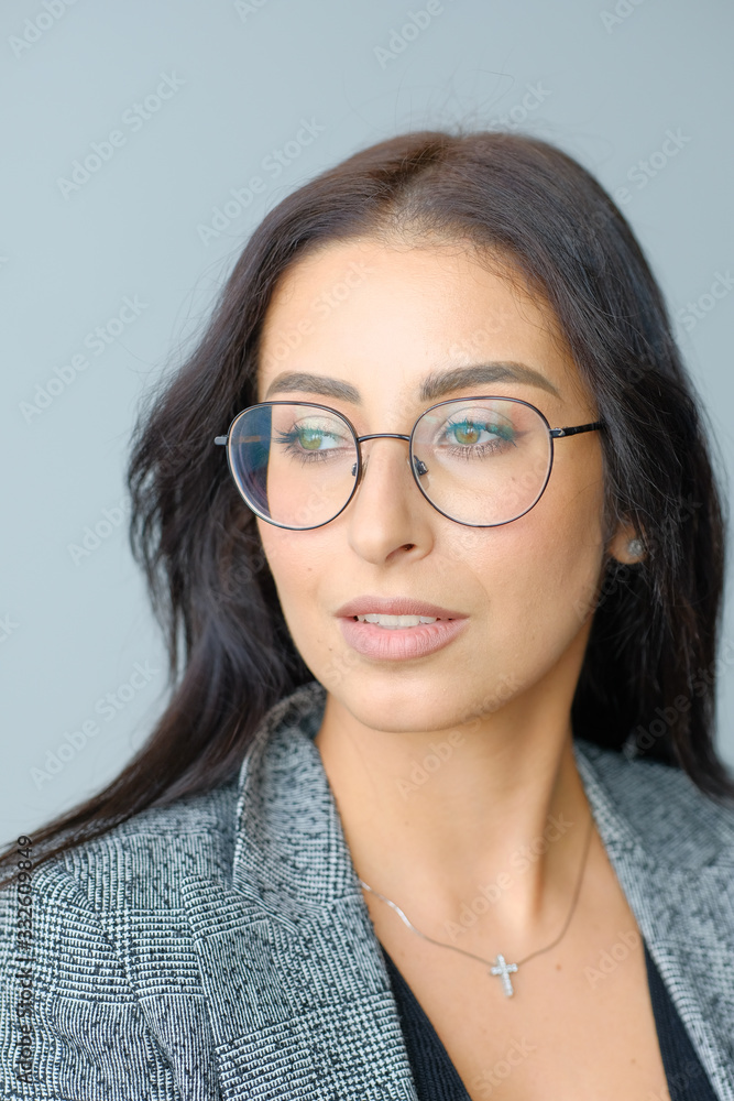 Portrait of a smiling mid-aged business woman with dark hair and brown eyes in glasses and a jacket against a light wall Portrait of a smiling mid-aged business woman with dark hair and brown eyes in glasses and a jacket against a light wall