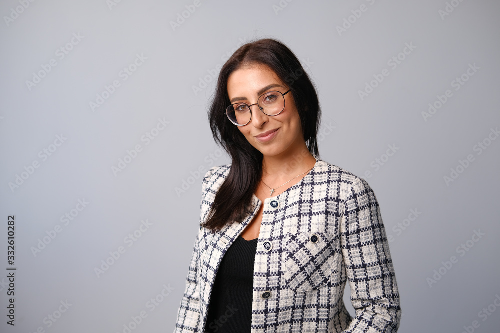 Fototapeta premium Portrait of a smiling mid-aged business woman with dark hair and brown eyes in glasses and a jacket against a light wall