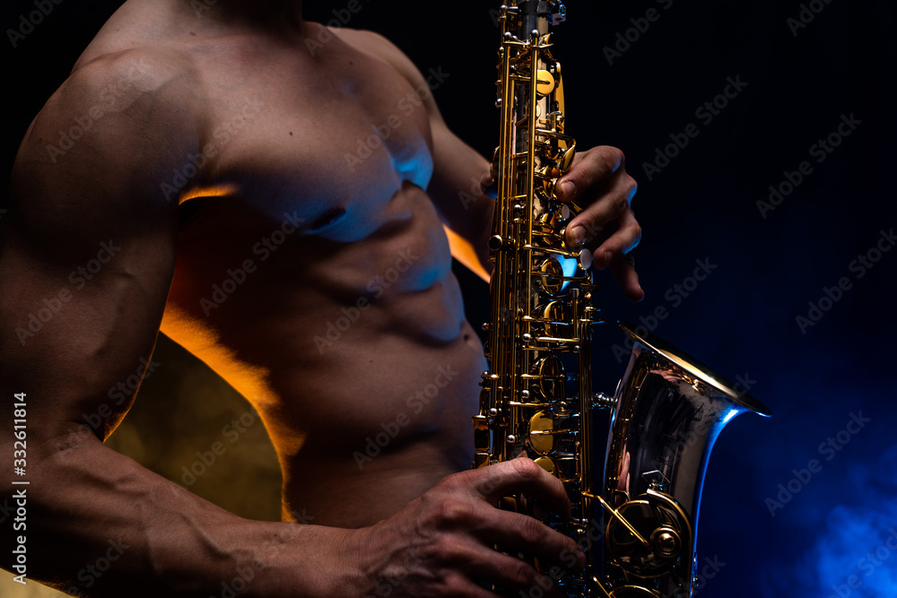 Fototapeta premium Muscular man with naked torso playing on saxophone with smoked colorful background 