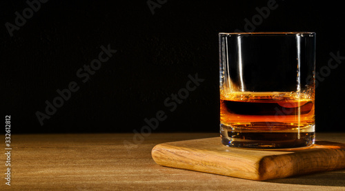 Glass with whiskey on wooden table and black background. Copy space. photo