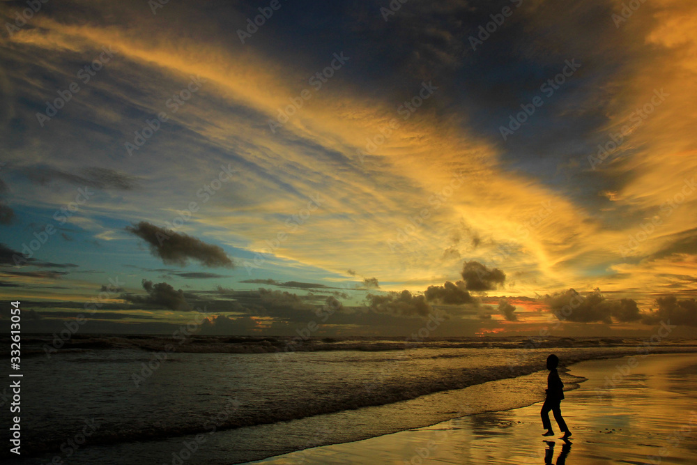 Obraz premium Silhouette boys play on the beach alone at dusk with dramatic sunset sky.