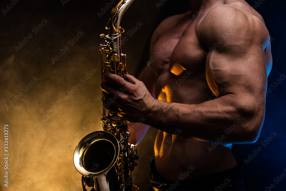 Obraz premium Muscular man with naked torso playing on saxophone with smoked colorful background