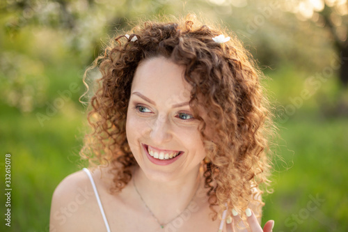 Close up portrait of young smiling attractive woman with curly hair in green flowering spring park. Pure emotions.