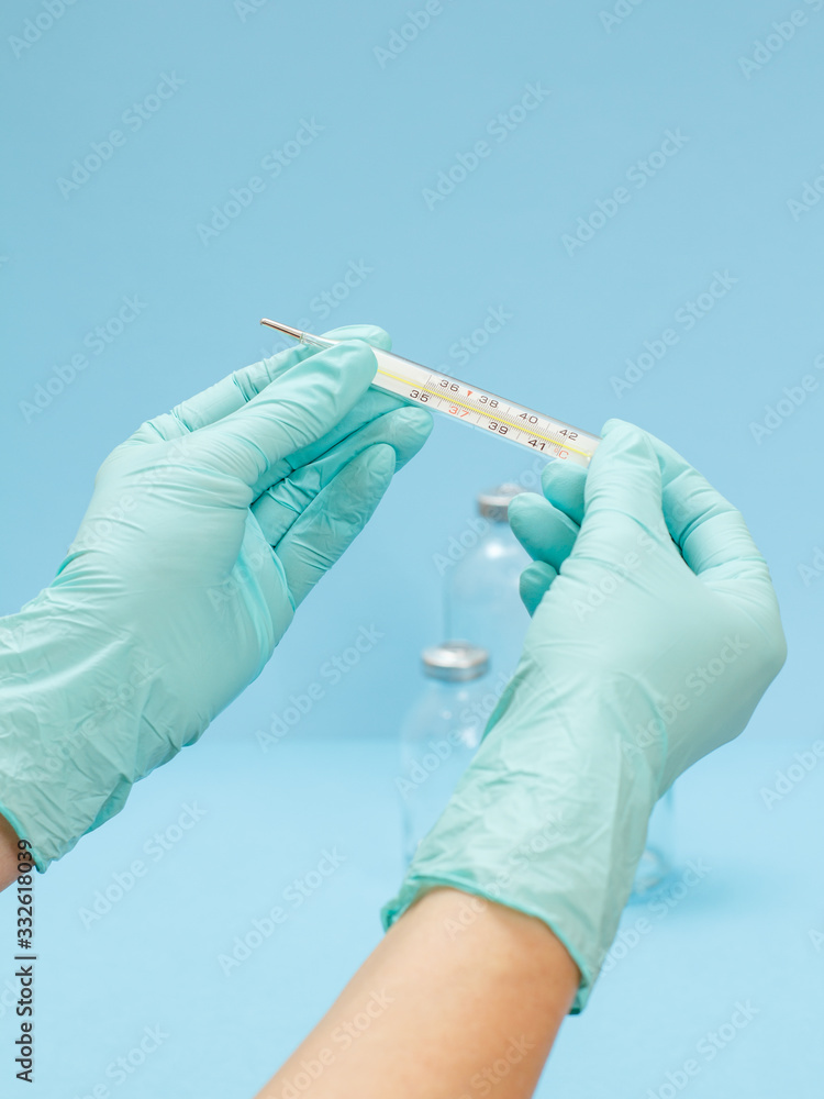 Fototapeta premium Doctor in latex gloves holding a glass mercury thermometer on blue background.