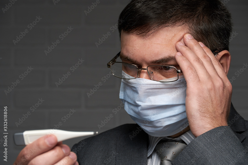 man measures body temperature with a thermometer, checks his health status, has a protective face mask - healthcare and medicine concept man measures body temperature with a thermometer, checks his health status, has a protective face mask - healthcare and medicine concept