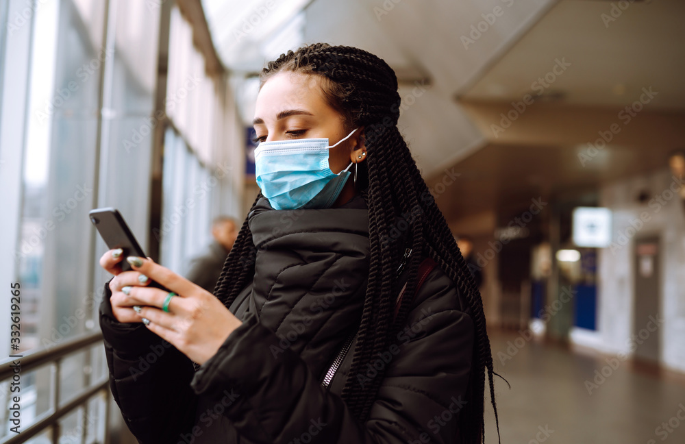 Girl in protective sterile medical mask on her face with a phone in quarantine city. Woman using the phone to search for news. The concept of preventing the spread of the epidemic. Girl in protective sterile medical mask on her face with a phone in quarantine city. Woman using the phone to search for news. The concept of preventing the spread of the epidemic.