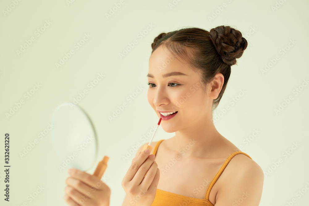 Beautiful young Asian woman applying lipstick over light background. Beautiful young Asian woman applying lipstick over light background.