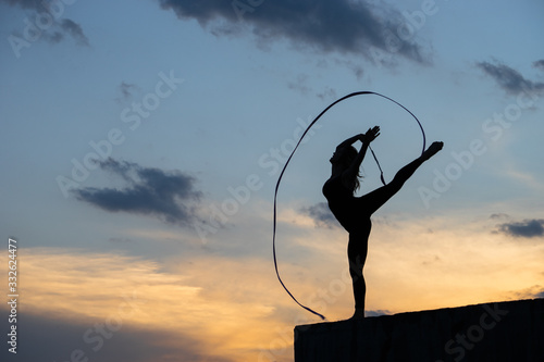 Professional gymnast woman dancer with ribbon on sky background