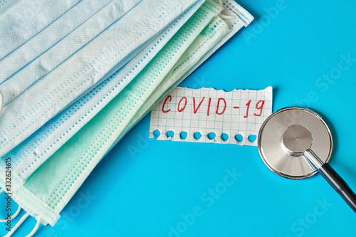 Medical masks. Medical protective masks on blue background with Stethoscope and Inscription COVID-19 on a piece of paper. Healthcare and medical concept.