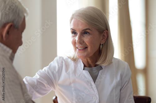 Friendly smiling mature doctor supporting, comforting older patient during visit close up, consulting about good medical checkup result, happy middle-aged nurse woman touching elderly man shoulder