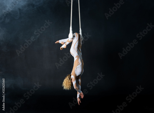 A young girl performs the acrobatic elements in the air trapeze. Studio shooting performances on a black background