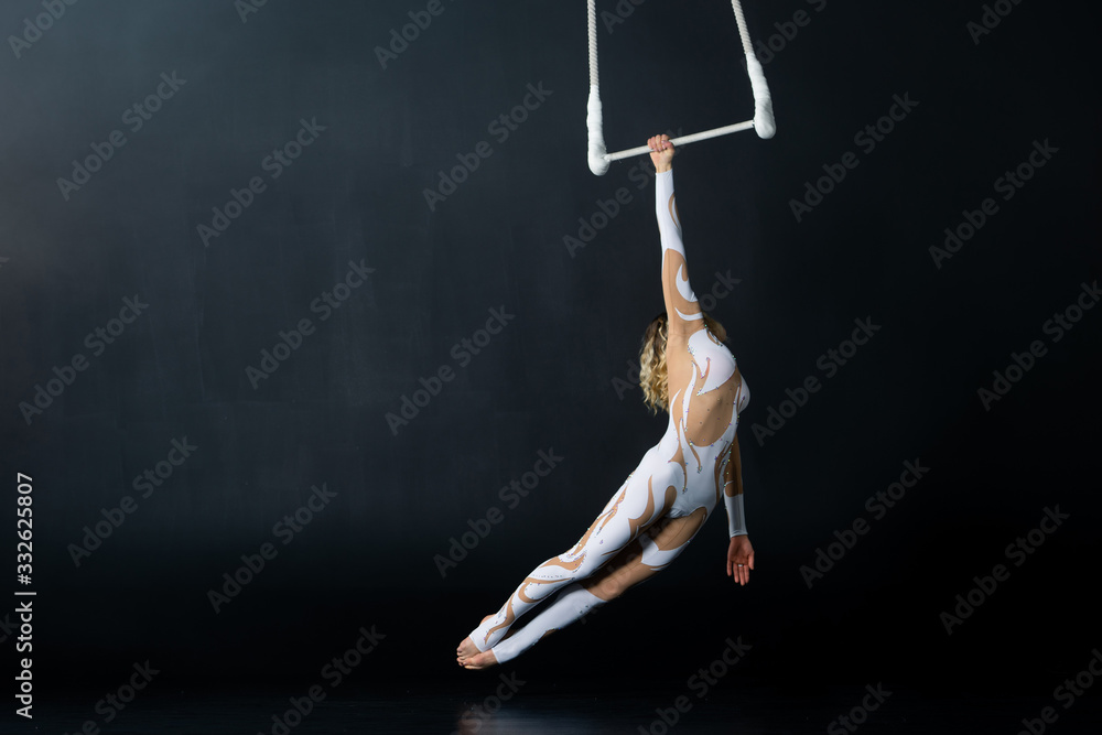 A young girl performs the acrobatic elements in the air trapeze. Studio shooting performances on a black background A young girl performs the acrobatic elements in the air trapeze. Studio shooting performances on a black background
