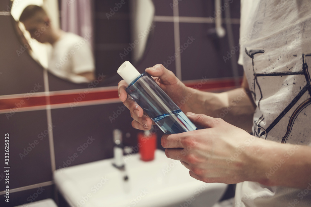 man with a bottle of liquid antibacterial soap in the bathroom . prevention of bacterial diseases and viruses