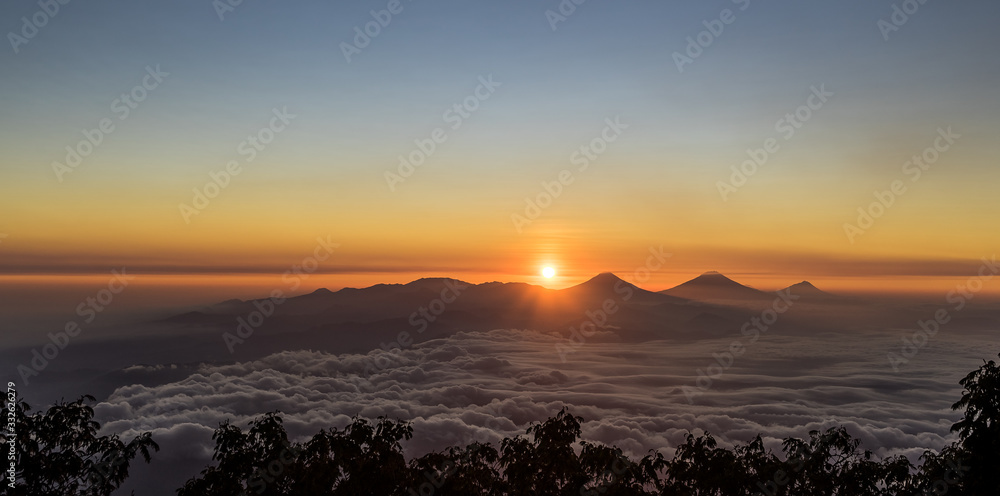 Wonderful remarkable sunrise with sea of clouds below Dieng plateau, Sumbing, Sindoro and Merbabu volcanoes seen from Slamet at 3200 meter above sea level altitude . Central Java, Indonesia