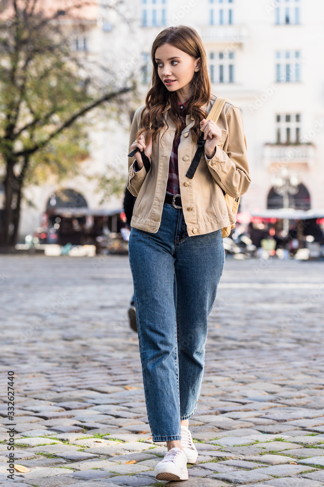 Fototapeta premium Beautiful woman looking away and walking with backpack in city