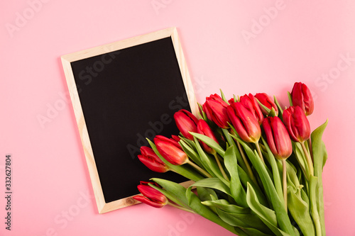 Black chalk board frame as a template with a bouquet of red tulips on a pink background. Beautiful festive blank for congratulation message, text or certificate.