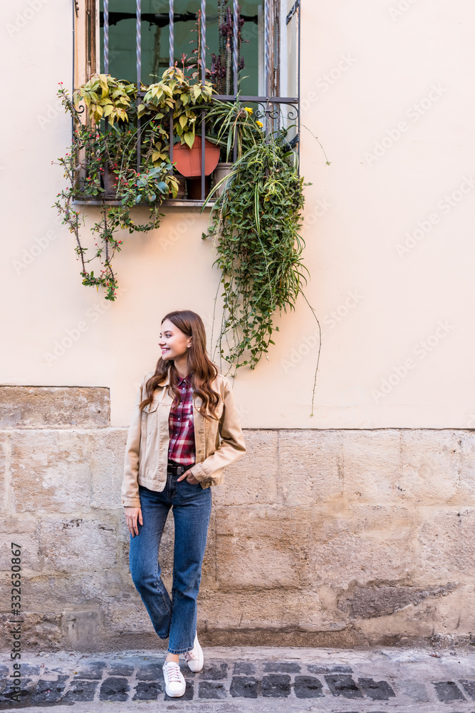 Full length view of girl with hand in pocket looking away near wall