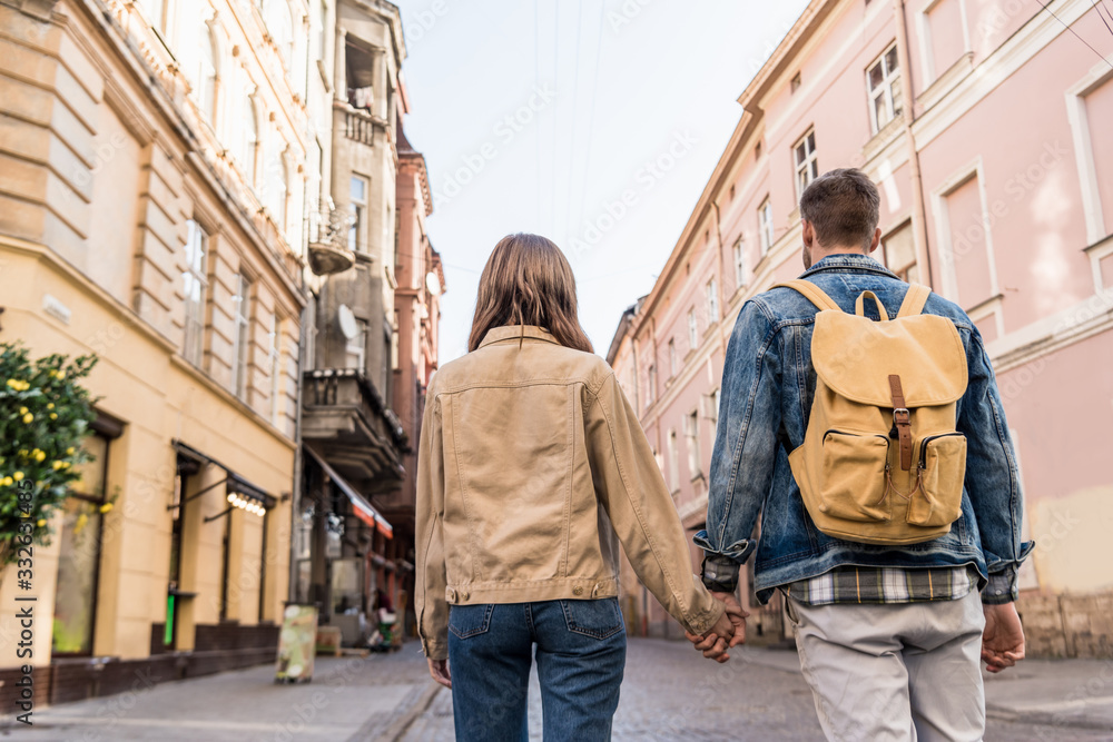 Back view of couple holding hands with backpack in city
