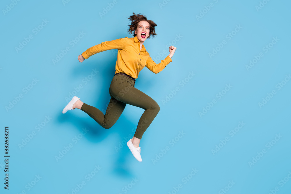 Full length profile photo of pretty lady jumping high up open mouth rushing shopping center wear yellow shirt green pants shoes isolated bright blue color background