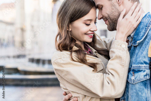 Partial view of woman and man hugging, smiling and touching each other with closed eyes