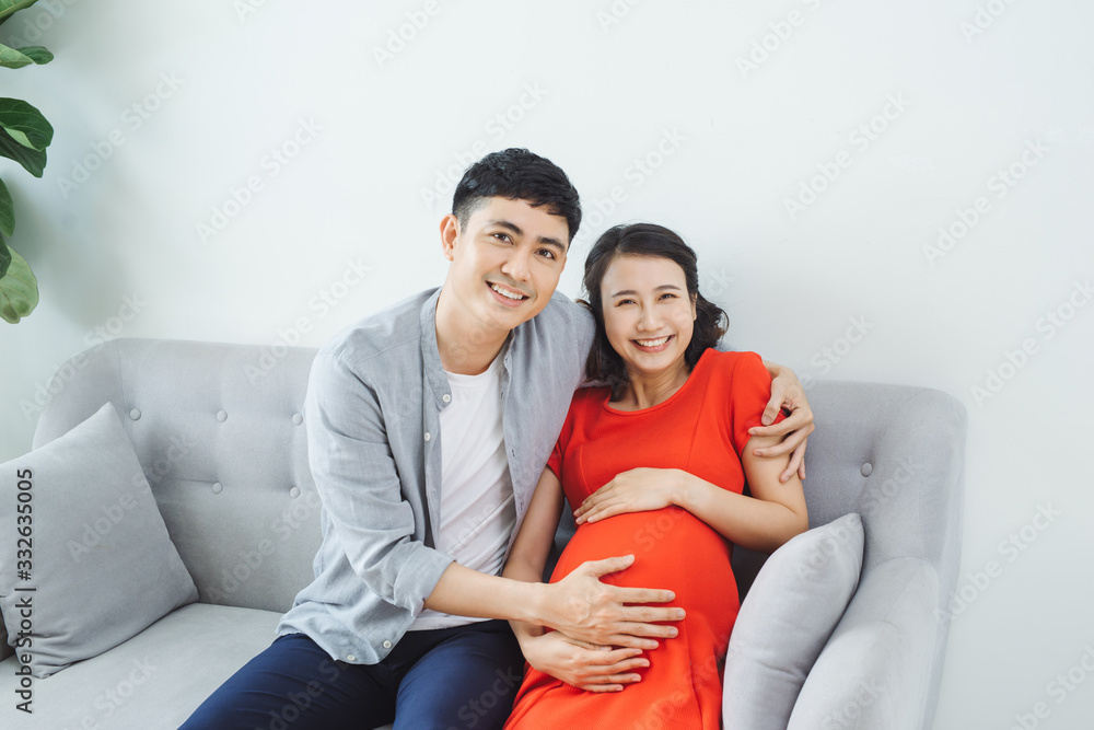 Fototapeta premium Young couple sitting on couch feeling baby kicking in mother's stomach