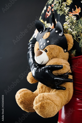 Bad Teddy Bear toy. woman in black latex gloves holds plush toy in leather mask and harness. photo