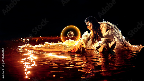 Beautiful white angel is standing in the water and looking at the rings of fire.