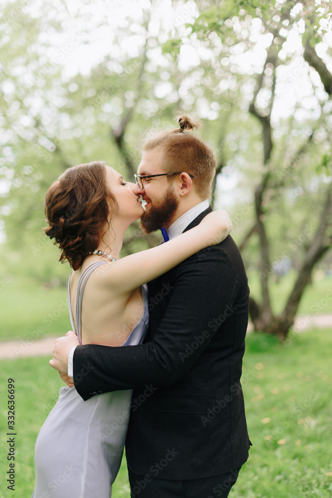 a young beautiful couple, a girl in a lilac dress and a man in black in a summer Park with Apple trees a young beautiful couple, a girl in a lilac dress and a man in black in a summer Park with Apple trees