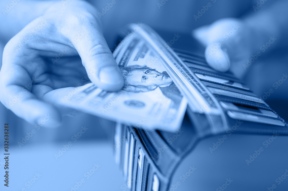 men's hands hold 20 dollar bills and a wallet on a blue table. toned in classic blue color trend 2020 year men's hands hold 20 dollar bills and a wallet on a blue table. toned in classic blue color trend 2020 year