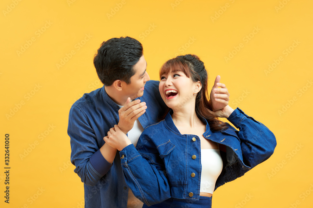 Couple playing hide and seek. Man standing behind his wife and closing her eyes, yellow background Couple playing hide and seek. Man standing behind his wife and closing her eyes, yellow background