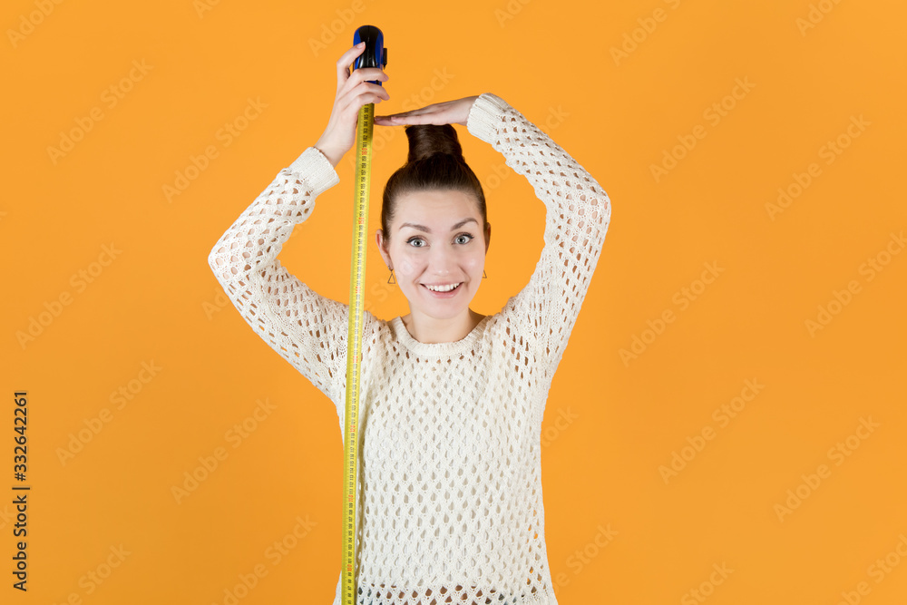 smiling adult girl holds measuring tape next to her and measures her height - obrazy, fototapety, plakaty 