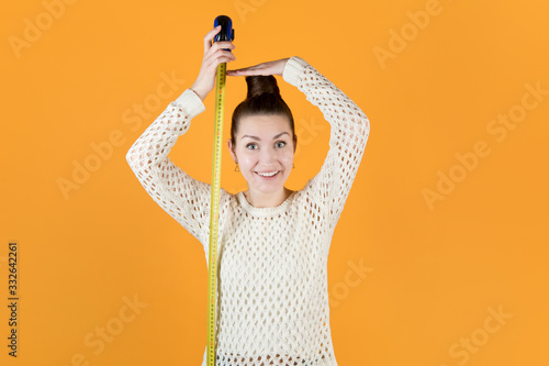 smiling adult girl holds measuring tape next to her and measures her height
