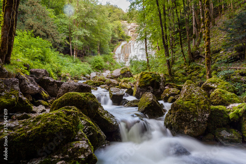 River flowing quickly in forest area, many mossy stones. Waterfall in back. France, Europe..
