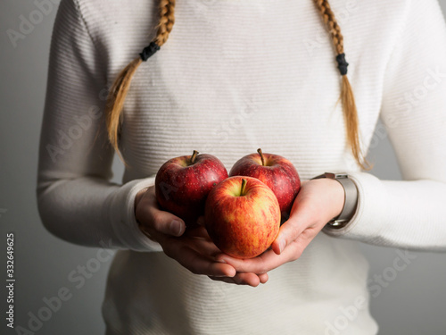 Junge Frau hält rote Äpfel in ihren Händen, geflochtene Zöpfe und weißer Pullover, gesunde Ernährung, Nahafunahme photo