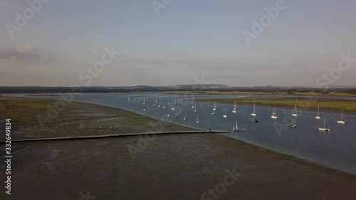 Flying over a harbour at low tide, with sailing boats anchored in.