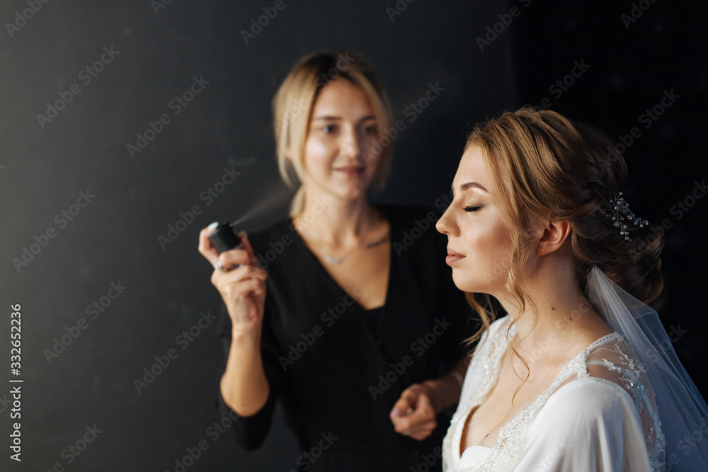 Plakat Portrait of professional hairdresser with hairspray in hands working with client. hairdresser makes wedding hairstyle to beautiful blonde bride studio portrait. evening hairstyle. beauty concept