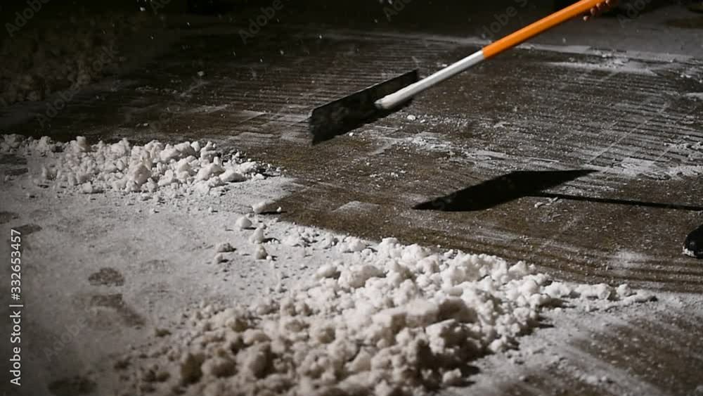 Janitors manually remove fresh snow from the sidewalk during snowfall at night time Janitors manually remove fresh snow from the sidewalk during snowfall at night time