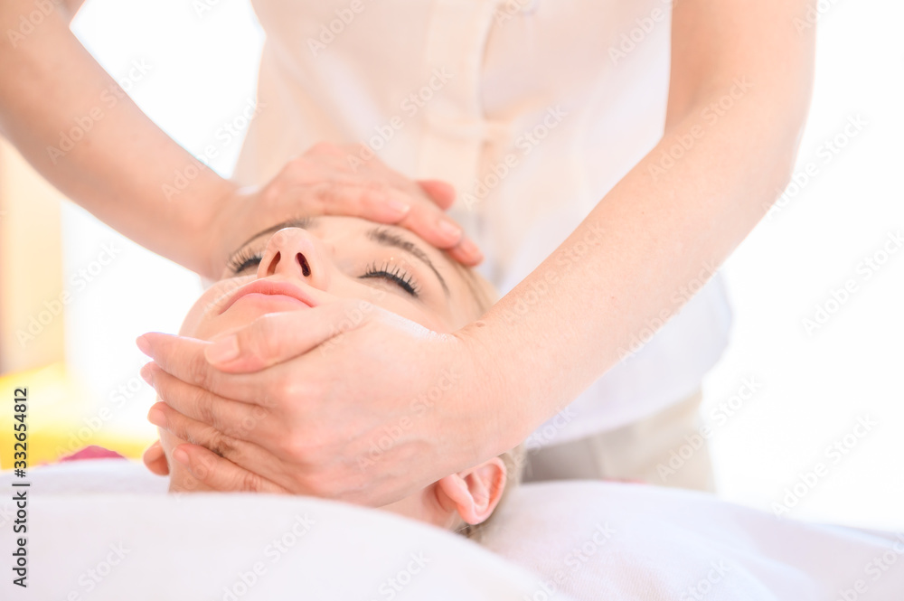 Fototapeta premium Beautiful woman receiving head and facial massage in spa salon. Concept of body health care and traditional thai massage relax