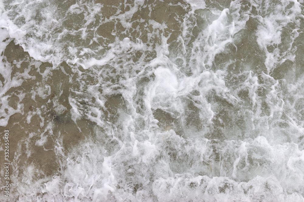 Top view texture waves, foaming and splashing in the ocean, sunny day.  Beautiful tropical sea in summer season image by aerial view. Abstract sea background. Ocean waves close-up.