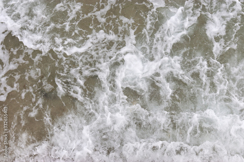 Top view texture waves, foaming and splashing in the ocean, sunny day. Beautiful tropical sea in summer season image by aerial view. Abstract sea background. Ocean waves close-up.