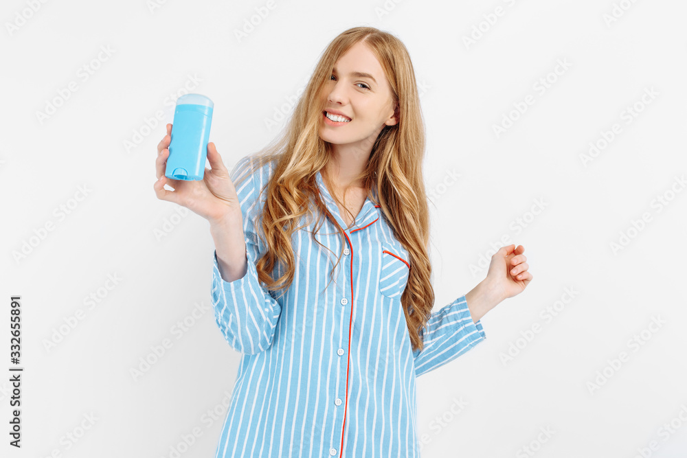 A girl in pajamas, holding a white bottle of deodorant to eliminate sweat, unpleasant odors. A young woman demonstrates an underarm antiperspirant after taking a shower A girl in pajamas, holding a white bottle of deodorant to eliminate sweat, unpleasant odors. A young woman demonstrates an underarm antiperspirant after taking a shower