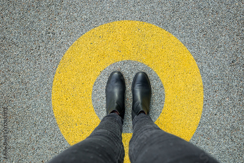 Black shoes standing in yellow circle on the asphalt concrete floor. Comfort zone or frame concept. Feet standing inside comfort zone circle photo